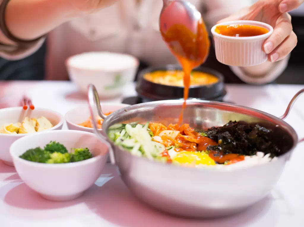 Un personne assaisonnant un bibimbap, plat coréen